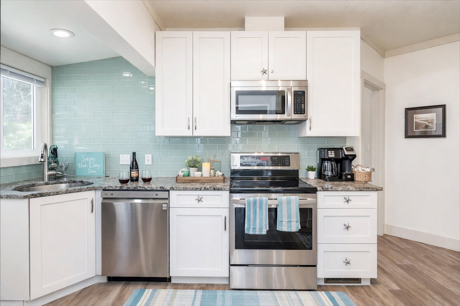 Fully equipped high-end kitchen with teal subway tile backsplash white shaker cabinets starfish hardware granite countertops stainless steel appliances and Seas the Day coastal decor at Anchor Court Beach House Lincoln City Oregon vacation rental