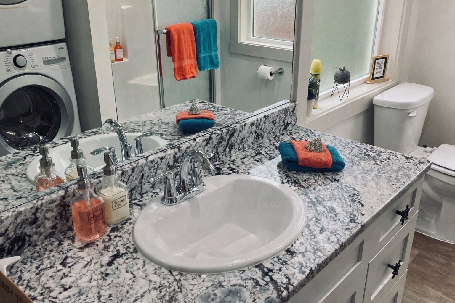 Primary bedroom suite bathroom with granite countertop chrome fixtures teal and coral towels washer dryer and coastal decor at Anchor Court Beach House Lincoln City Oregon vacation rental